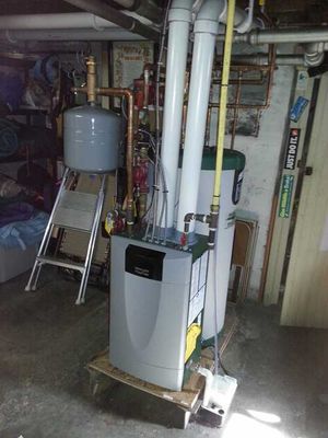 A boiler is sitting on top of a wooden table in a basement.