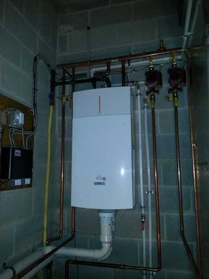 A white boiler is hanging from the ceiling in a room with copper pipes.