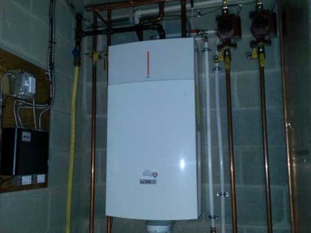 A white boiler is sitting in a room with copper pipes.