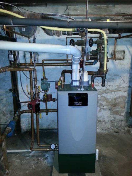 A boiler is sitting in a basement surrounded by pipes.