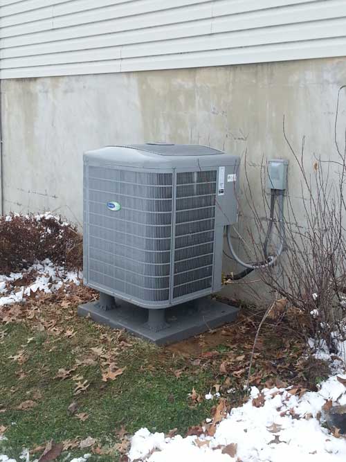 A gray air conditioner is sitting outside of a house.