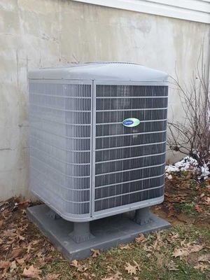 A large air conditioner is sitting on top of a concrete platform in front of a house.