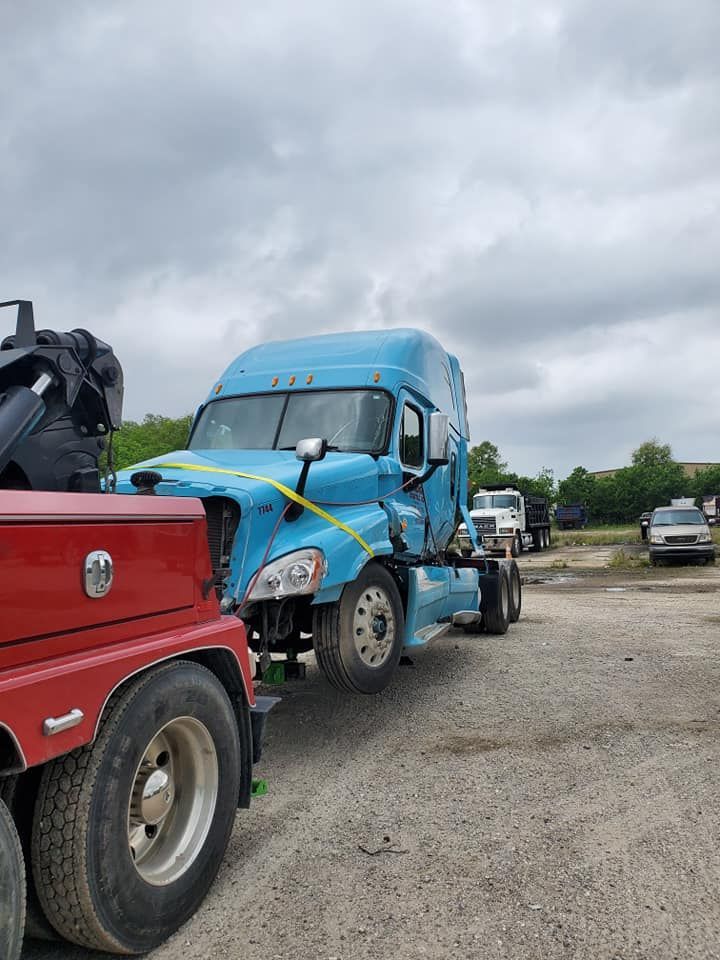 A blue semi truck is being towed by a red tow truck.