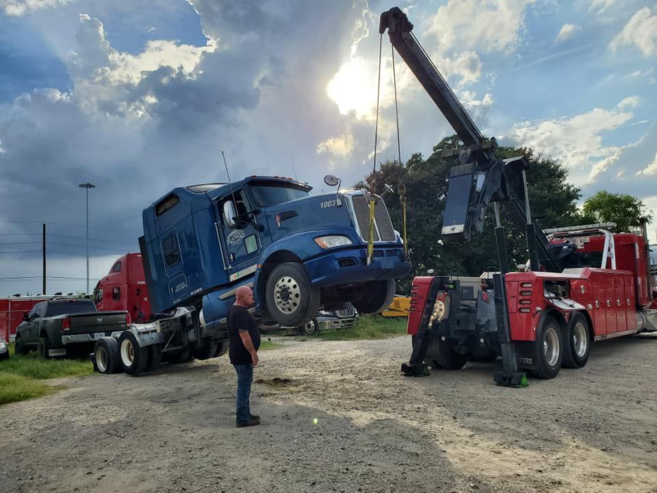 A man is standing next to a truck that is being towed by a crane.