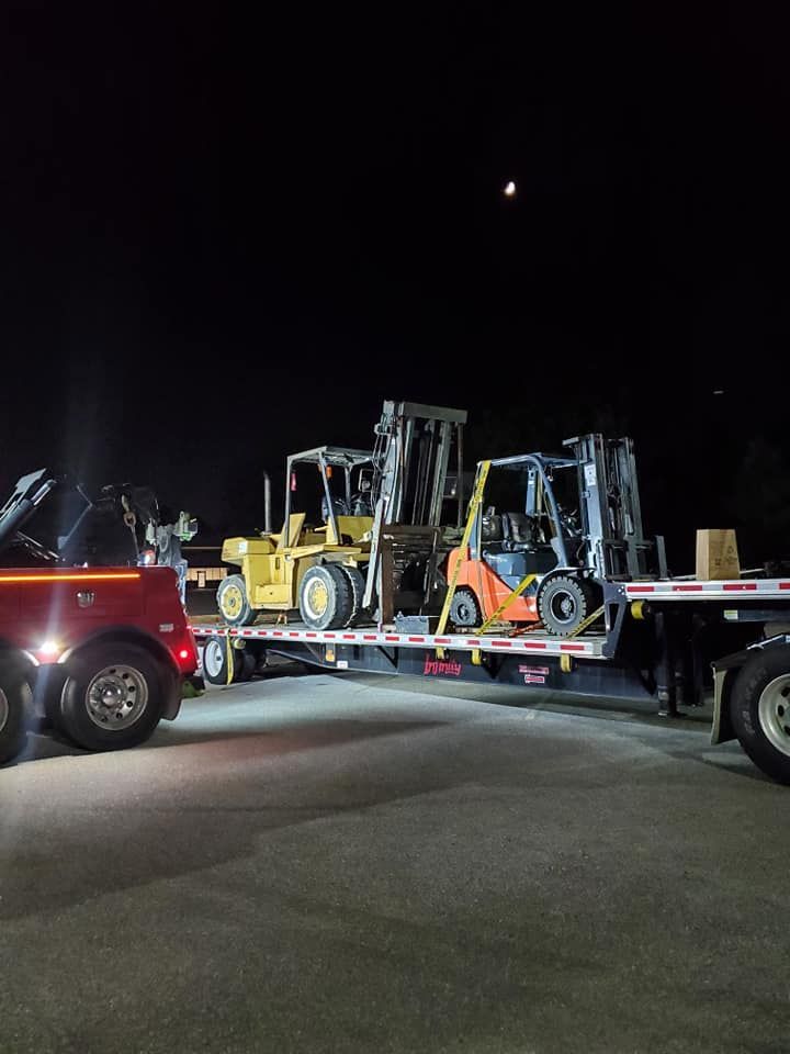 Two forklifts are being towed by a tow truck at night.
