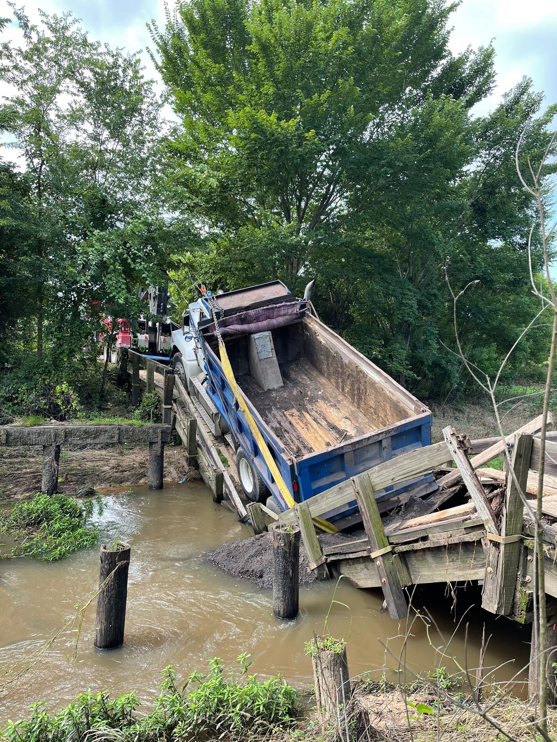 A dump truck is sitting on top of a wooden bridge in the water.