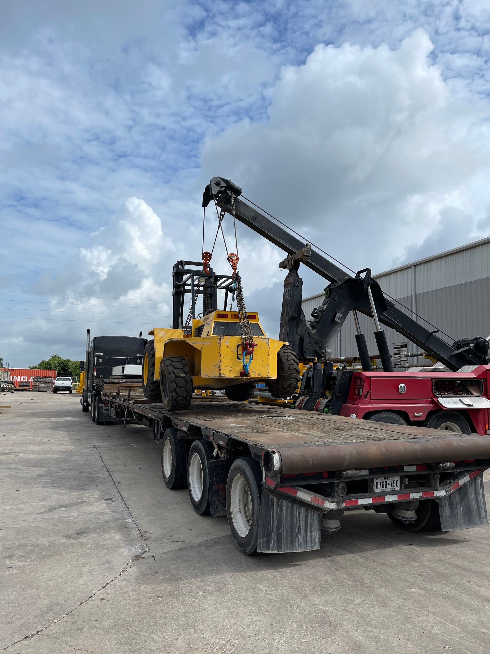 A yellow forklift is sitting on top of a flatbed trailer.