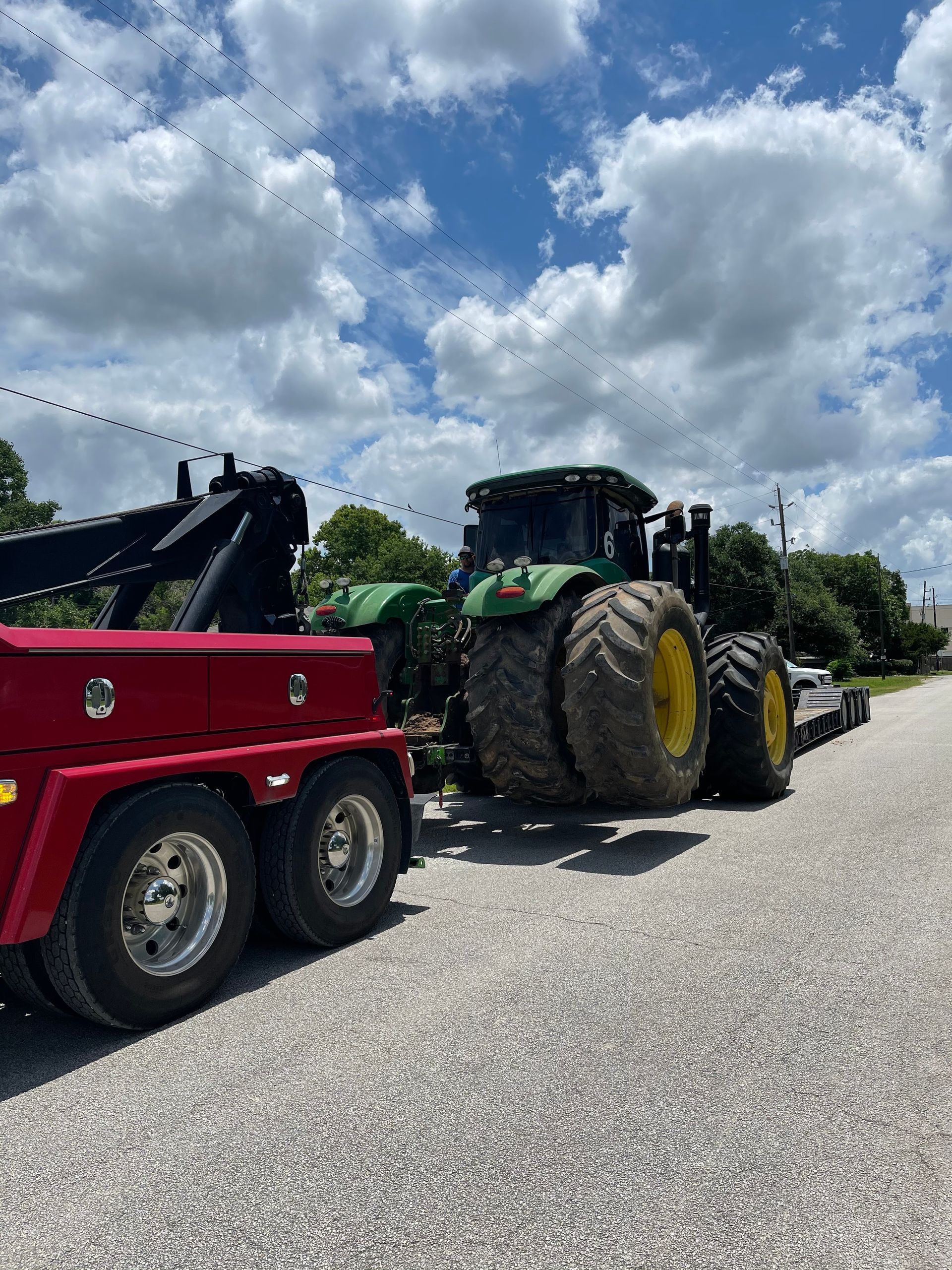 A red tow truck is towing a green tractor down a gravel road.