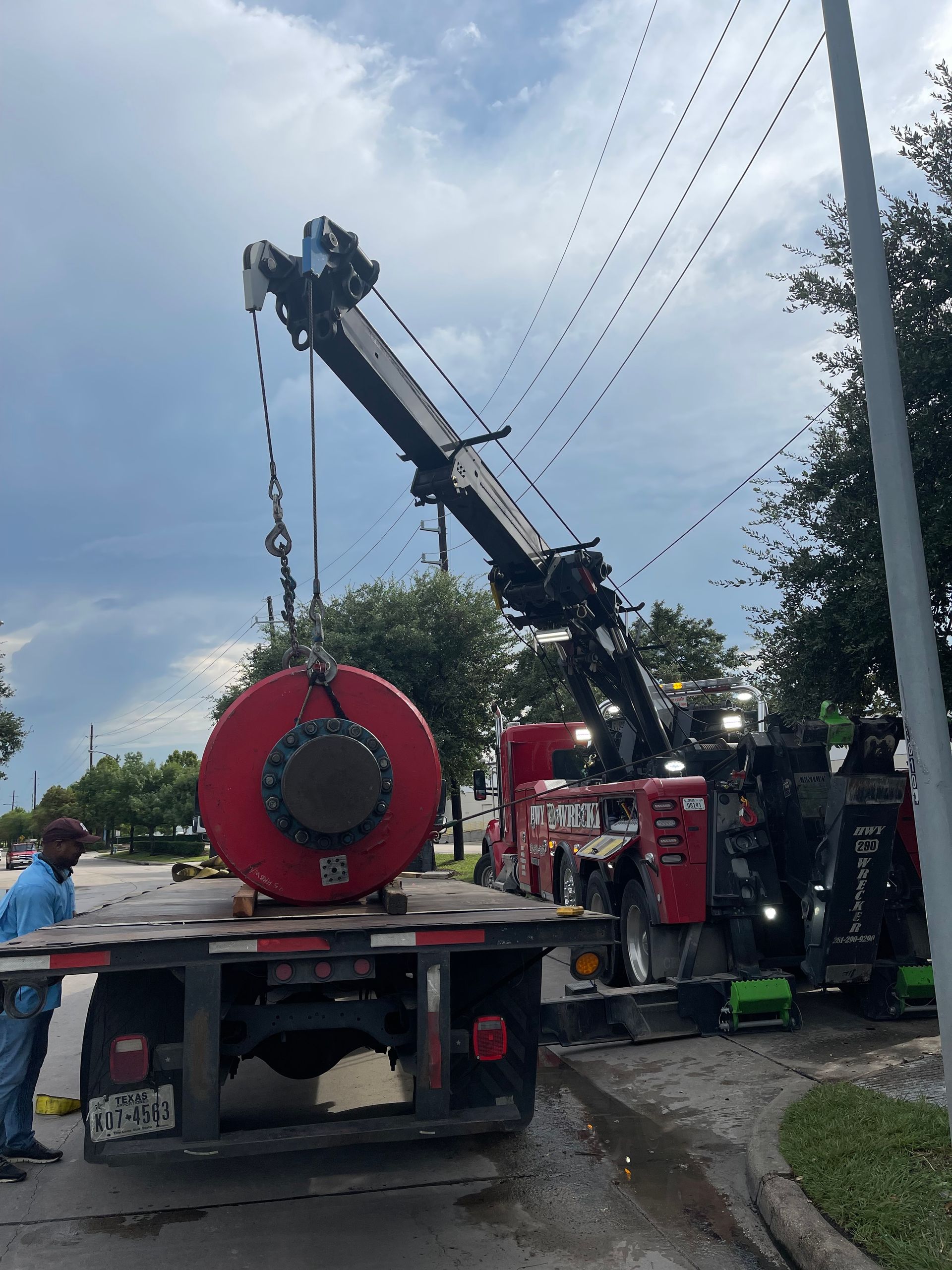 A crane is lifting a large red object from the back of a truck.