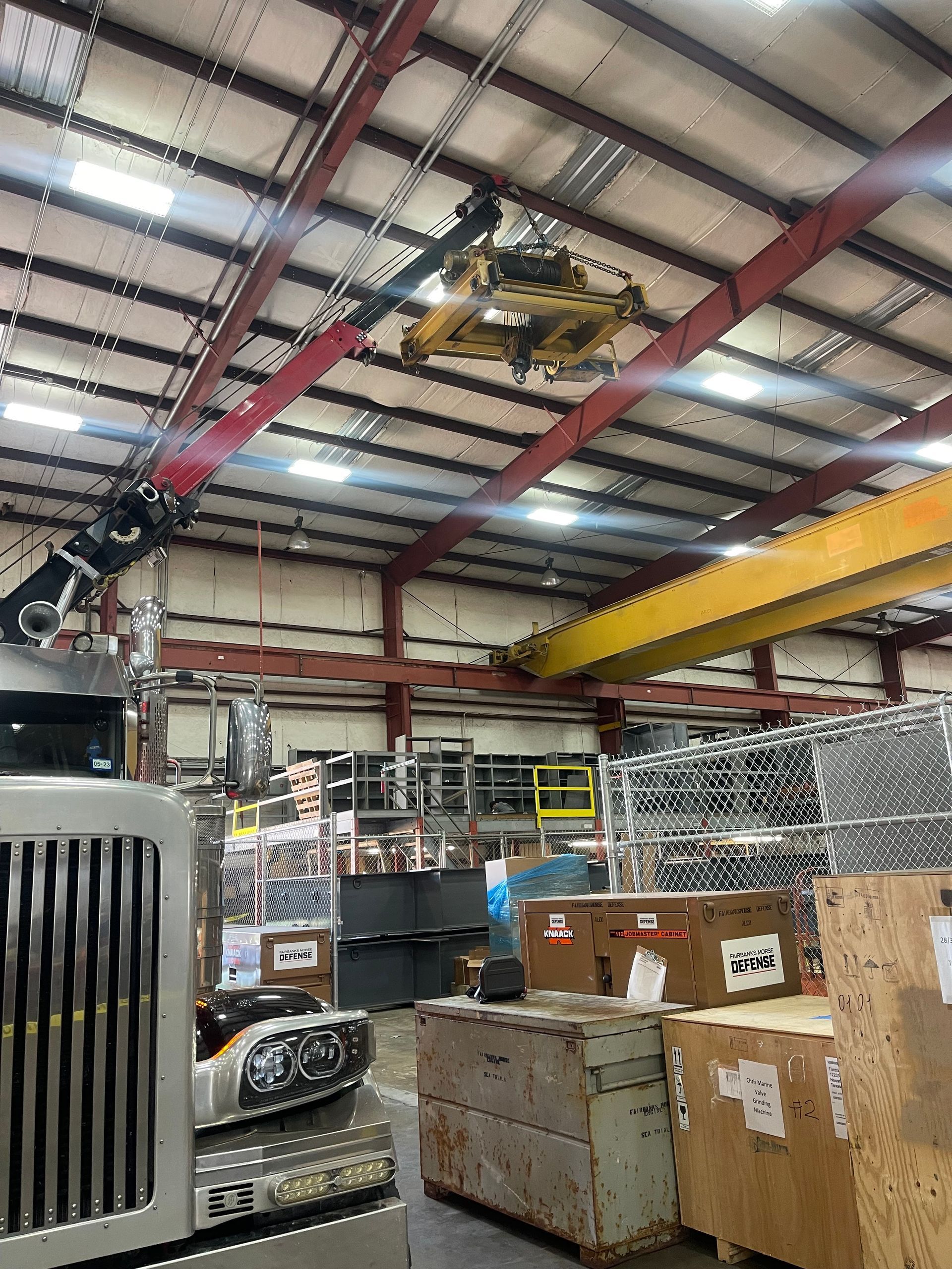 A truck is parked in a warehouse with a crane hanging from the ceiling.