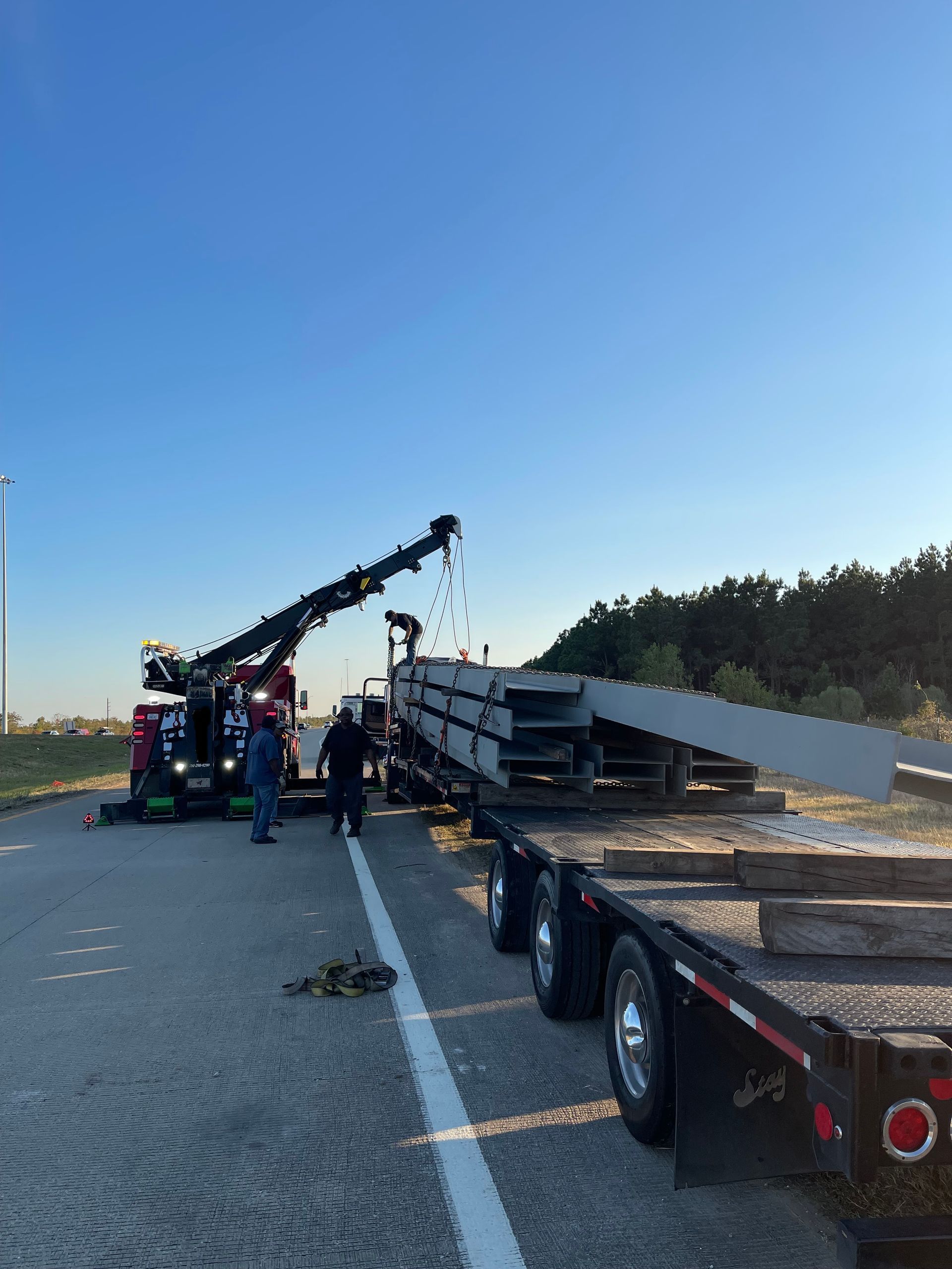 A truck is carrying a roller on the back of it on a highway.