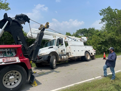 A man is standing next to a tow truck on the side of the road.