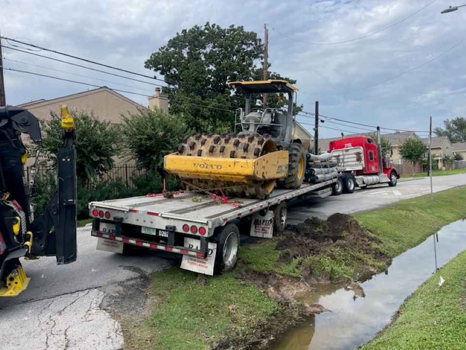A tow truck is carrying a tractor on a flatbed trailer.