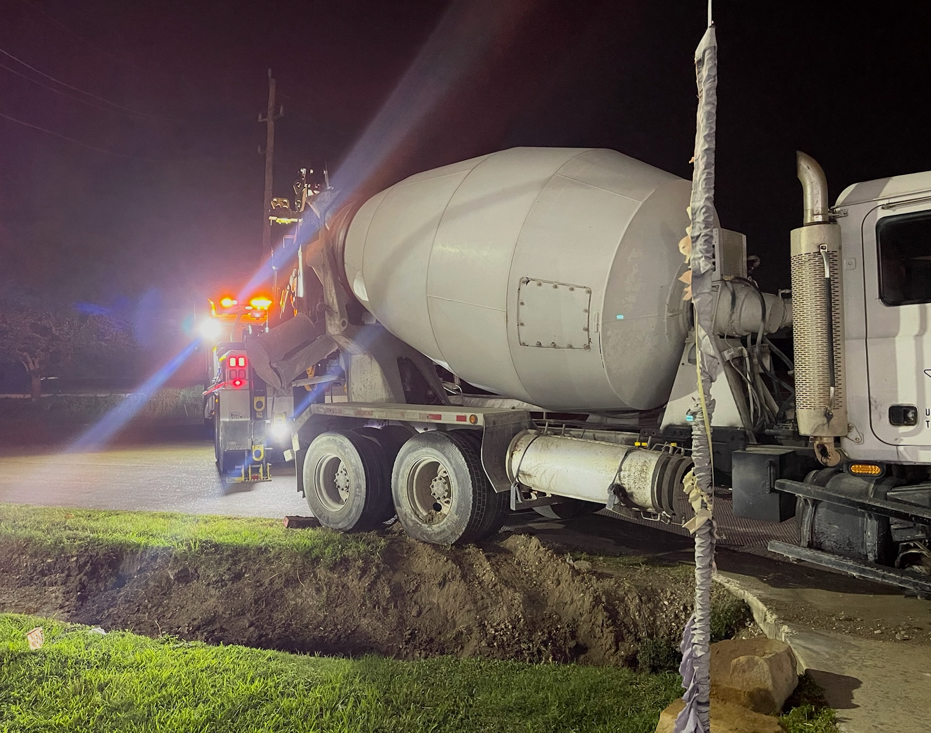 A concrete mixer truck is parked on the side of the road at night.
