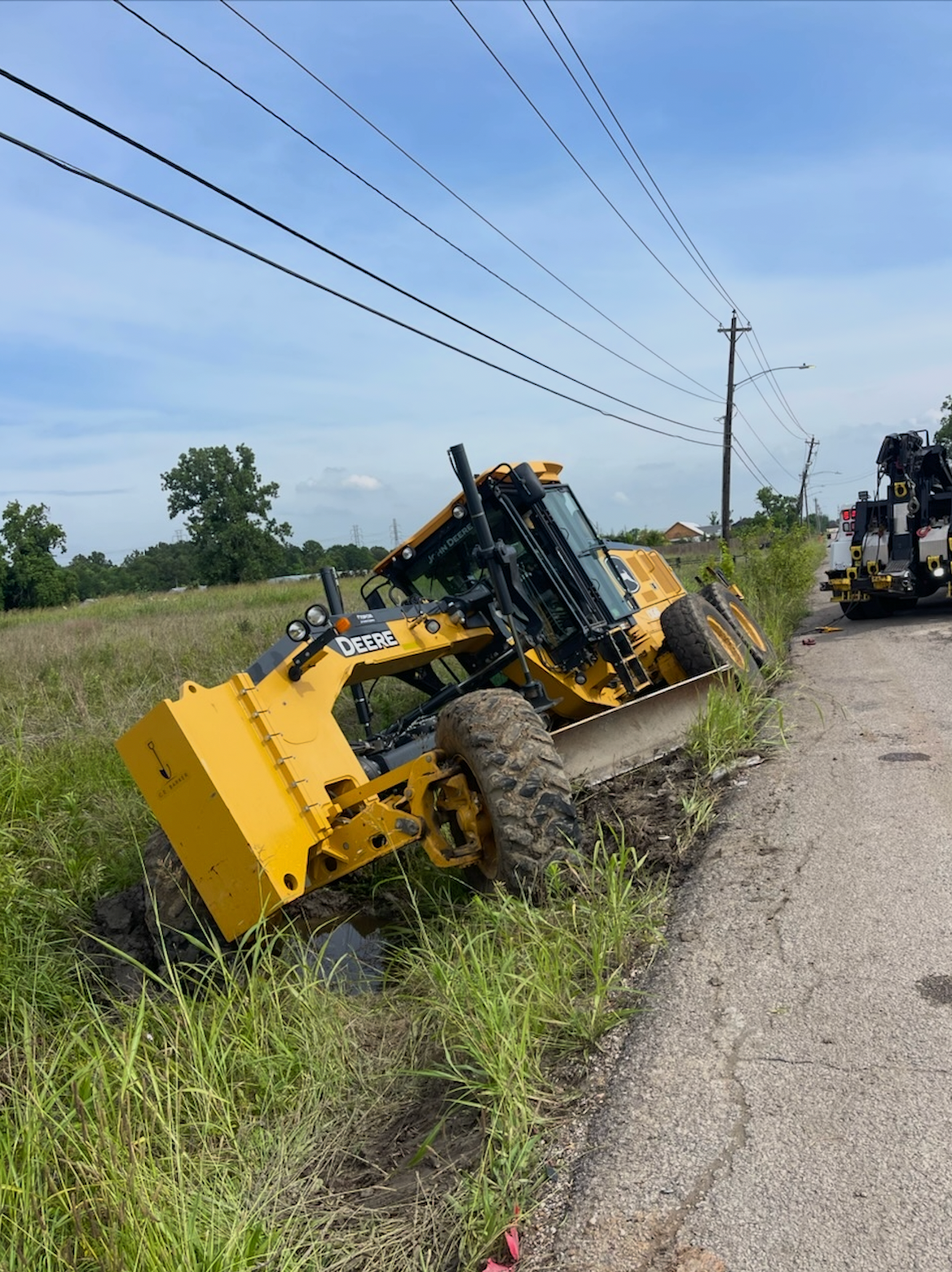 A yellow tractor is laying on its side on the side of the road.