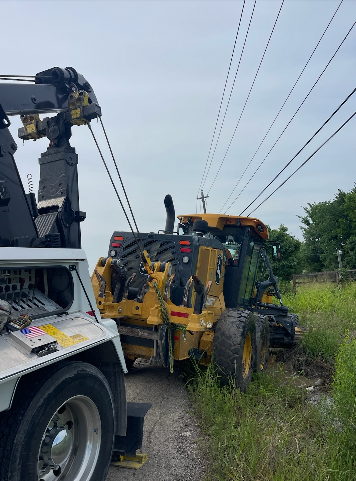 A tow truck is towing a tractor that is stuck on the side of the road.