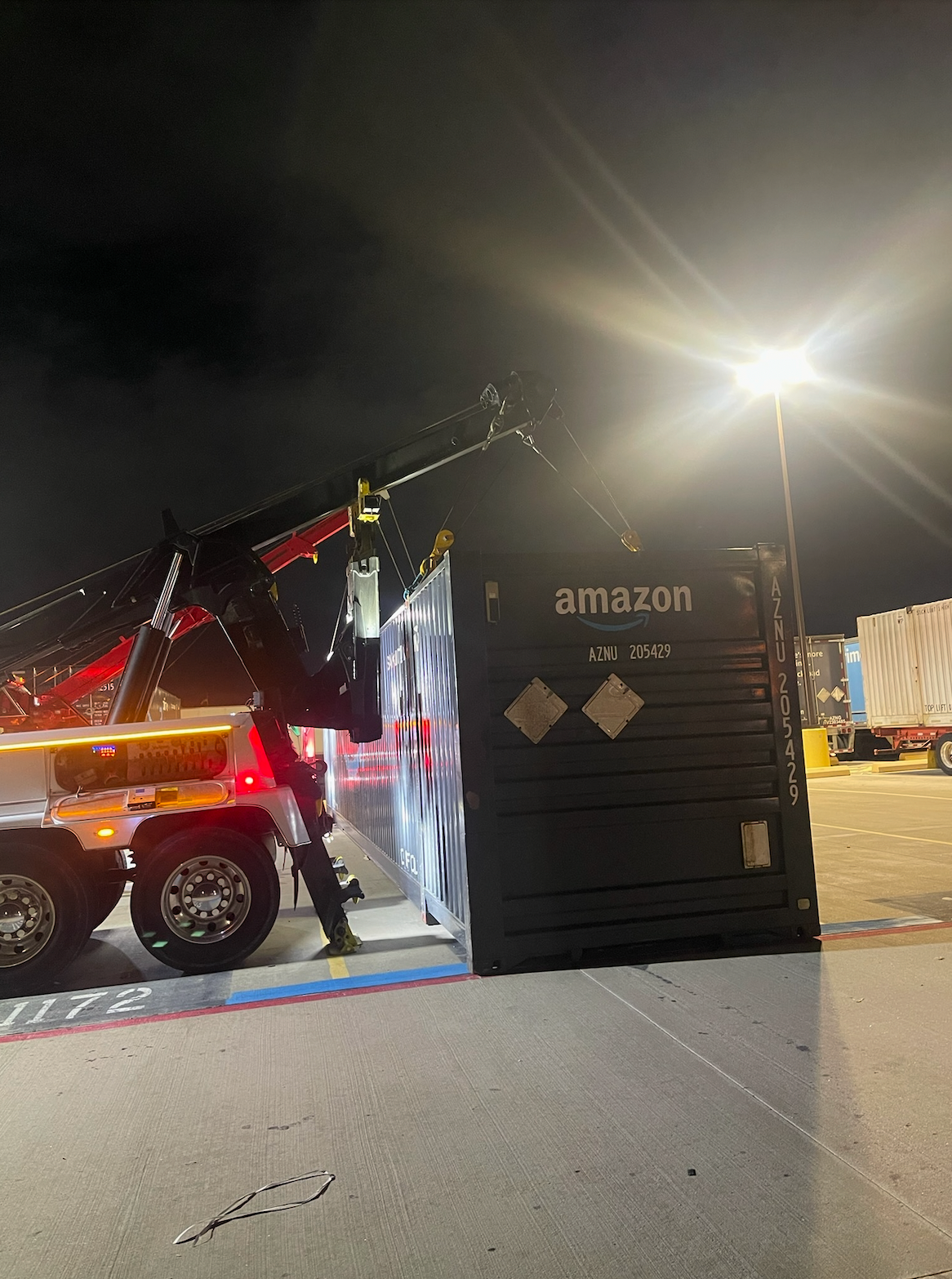 An amazon shipping container is being towed by a tow truck at night.