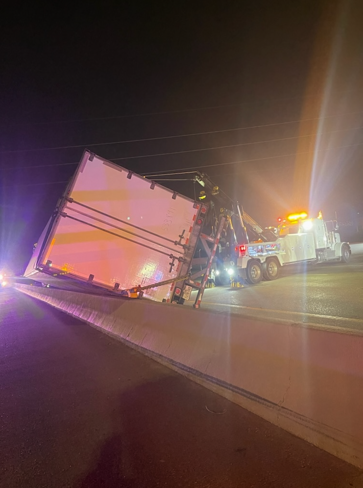 A tow truck is towing a semi truck that has fallen off the road.