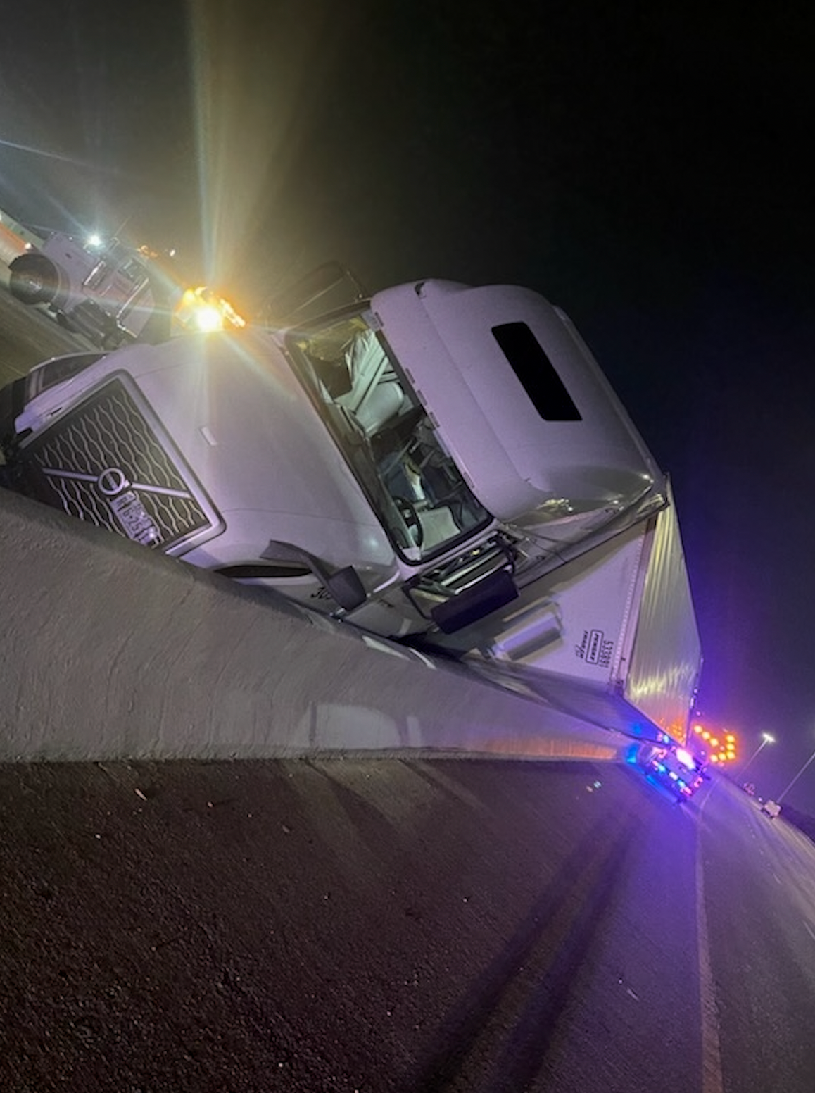 A white semi truck is turned over on the side of the road.