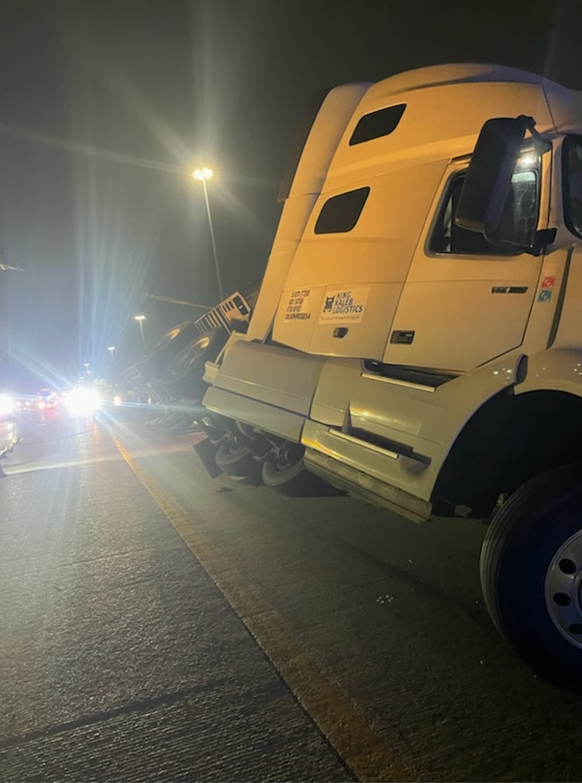 A white semi truck is parked on the side of the road at night.