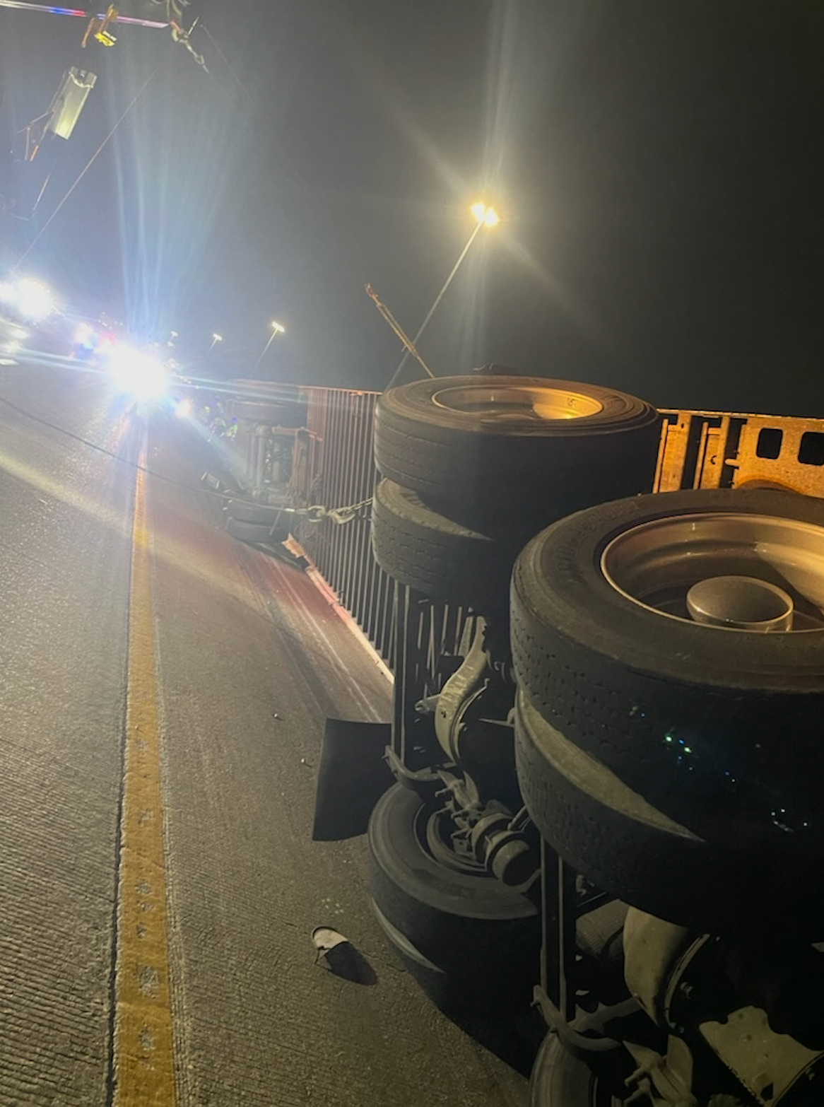 A truck is turned over on the side of the road at night.