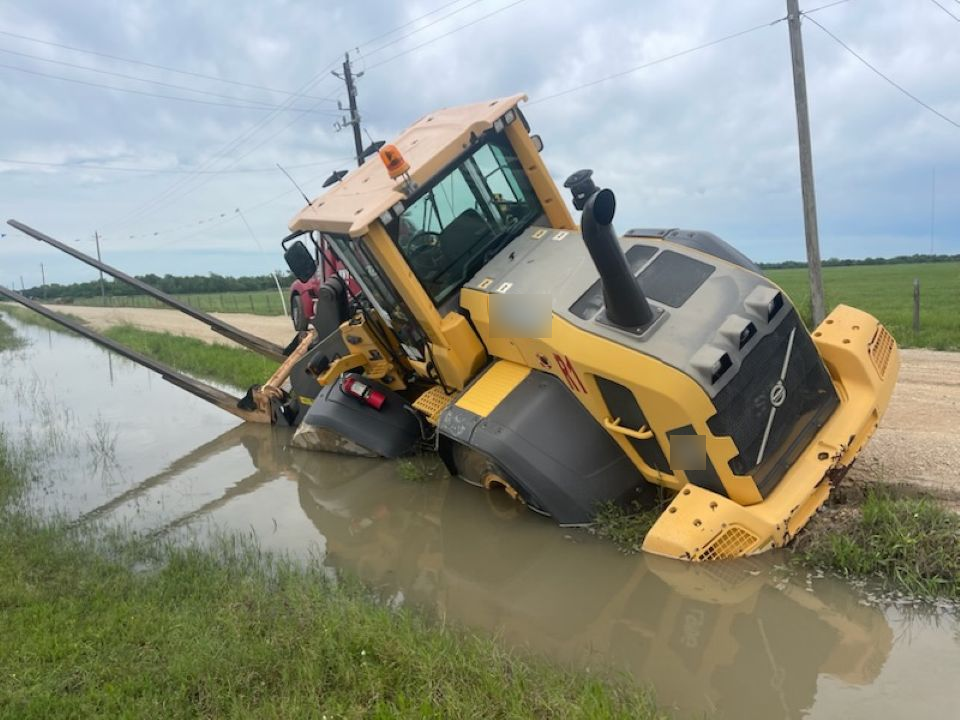 A yellow volvo tractor is stuck in a puddle of water