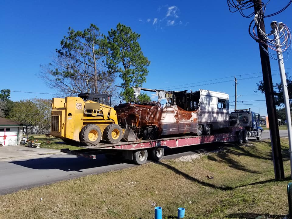 A tow truck is carrying a yellow tractor and a white truck.