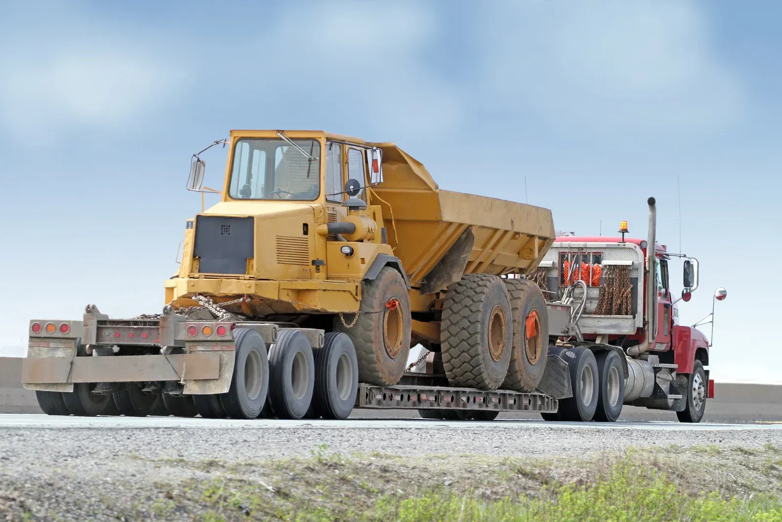 A semi truck is carrying a large dump truck on a trailer.
