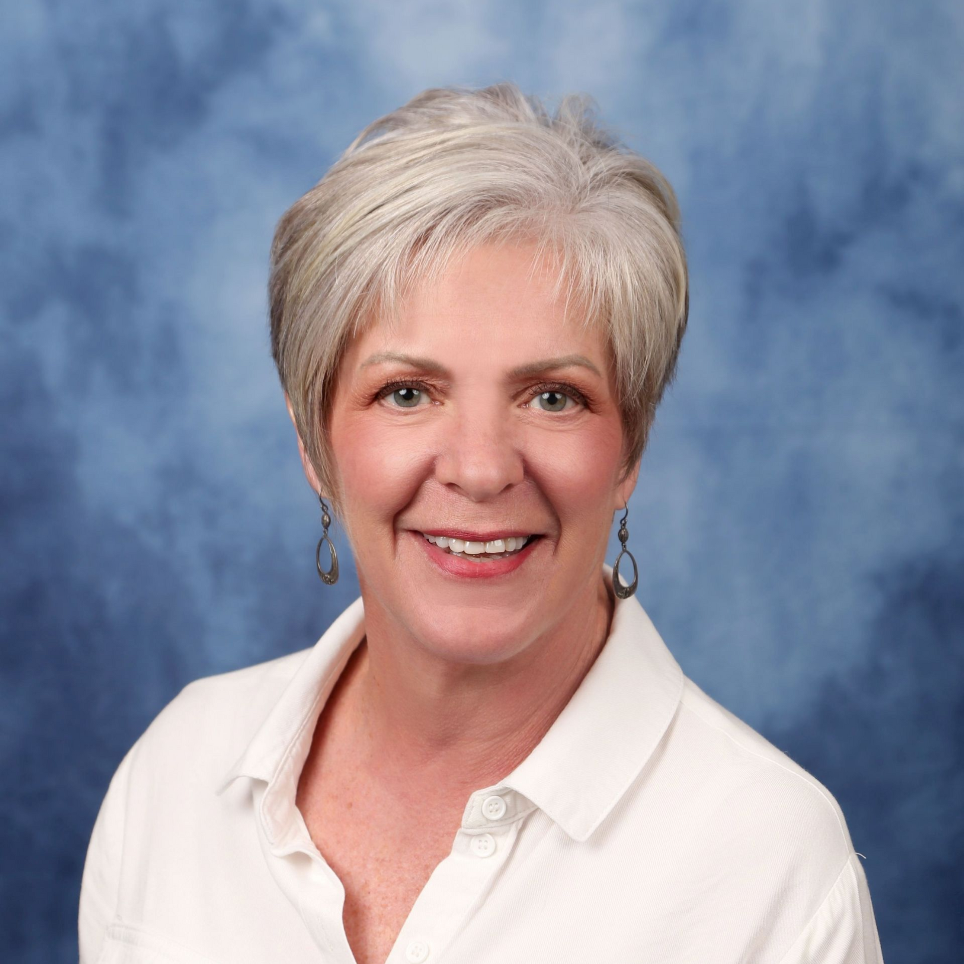 Man in a navy blazer and white shirt smiles broadly in a well-lit indoor setting.