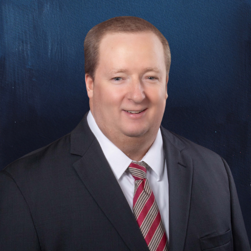 Man in a suit and tie, smiling, against a blue backdrop.