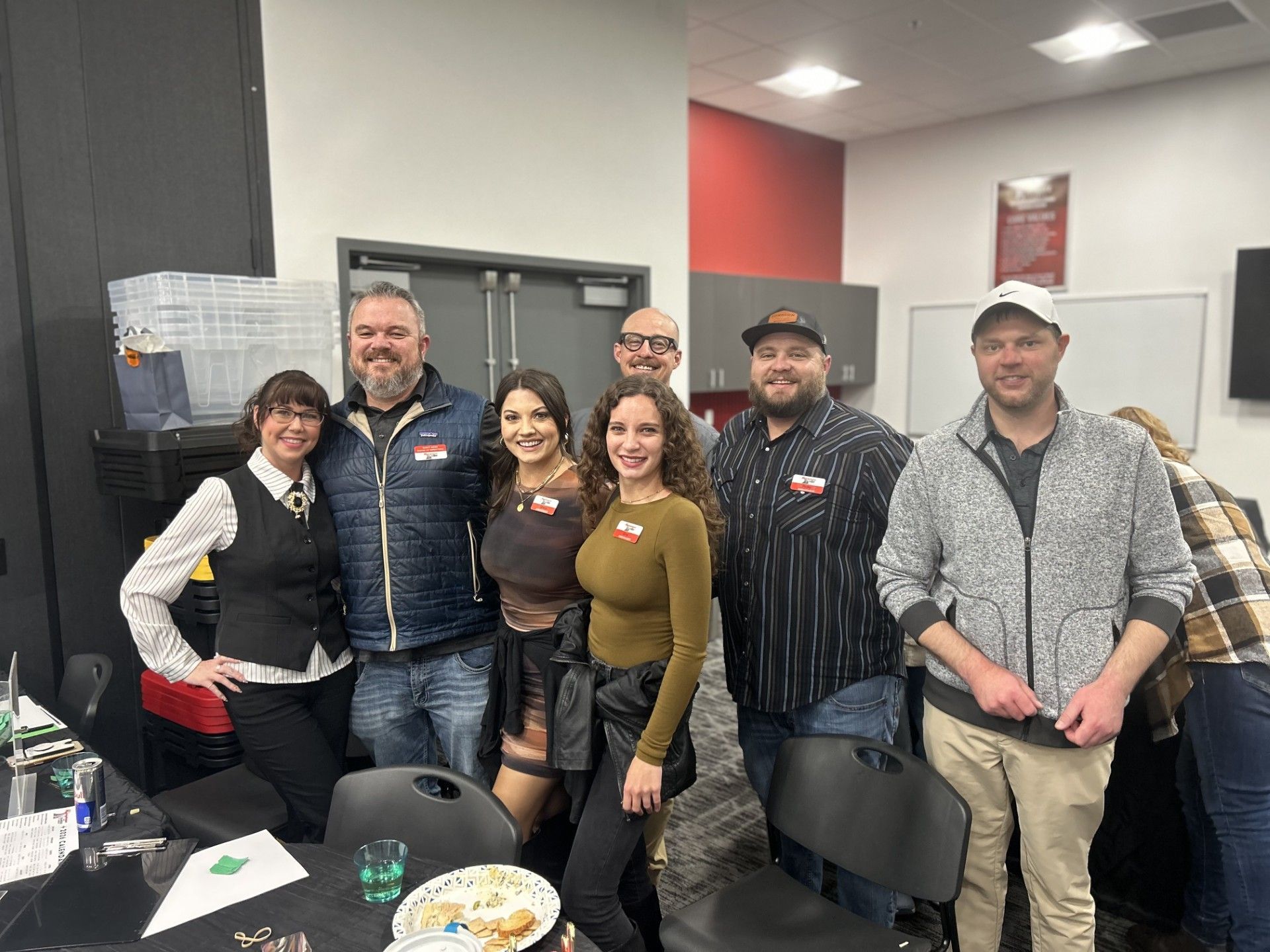 Group of people at an event, smiling. Interior setting with tables, food, and decorations.