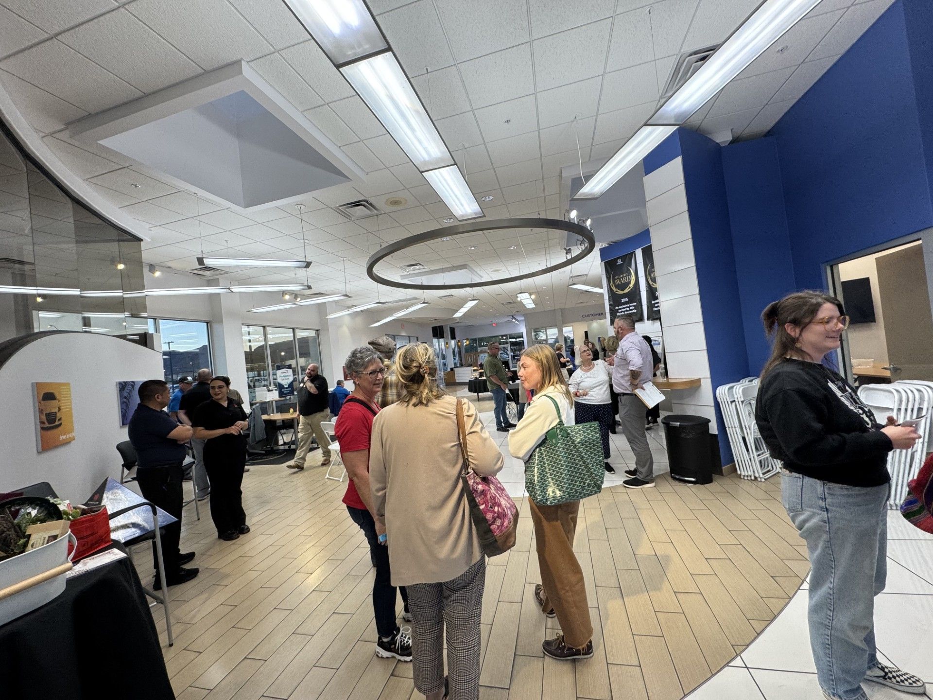 People gather indoors, some conversing. Bright, modern space with blue walls and wood floors.
