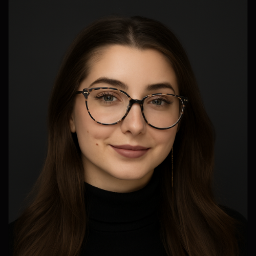 Woman with glasses and dark turtleneck smiles against a dark background.