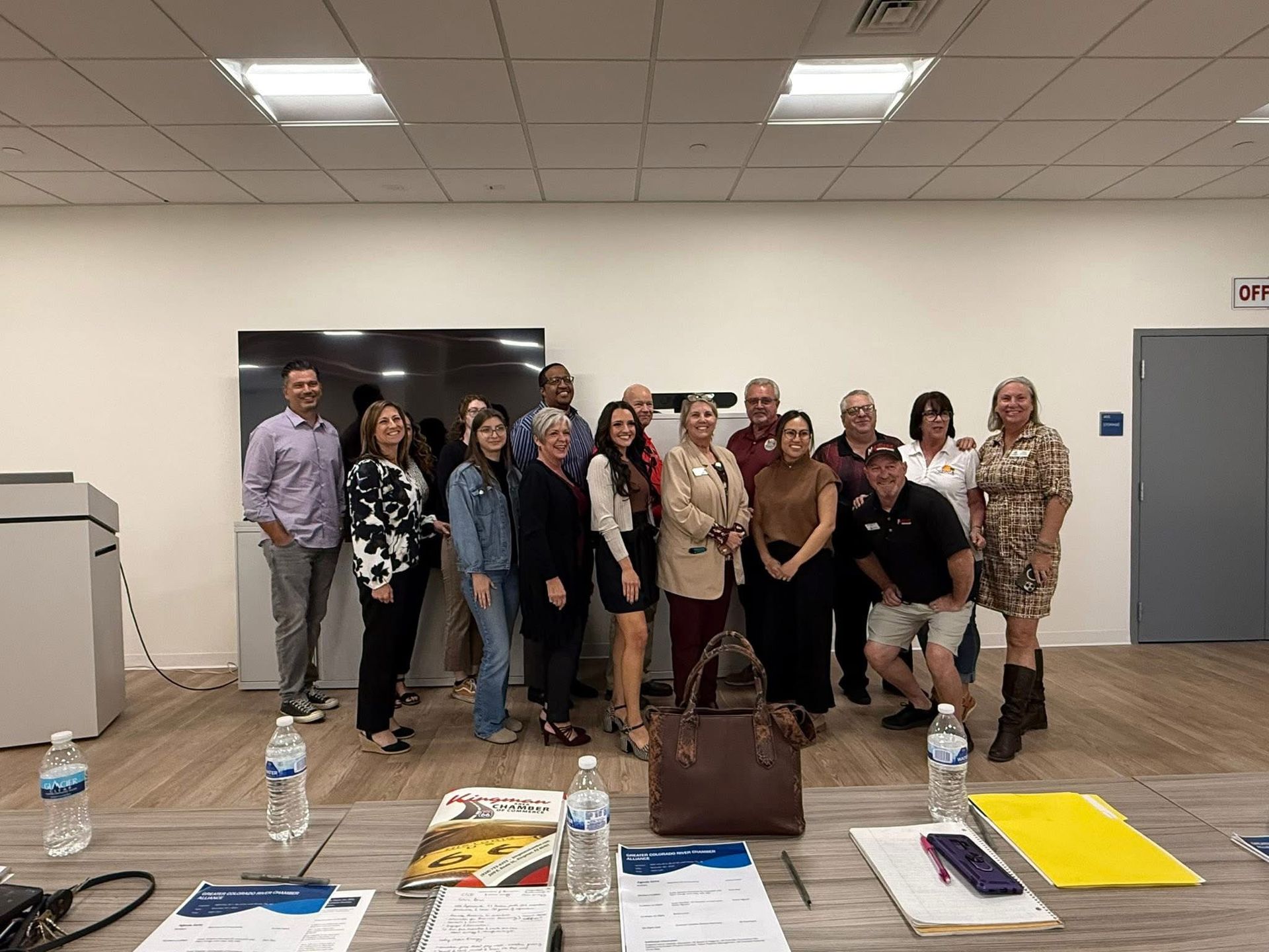 Group of people posing together in a brightly lit room with a table in front of them.