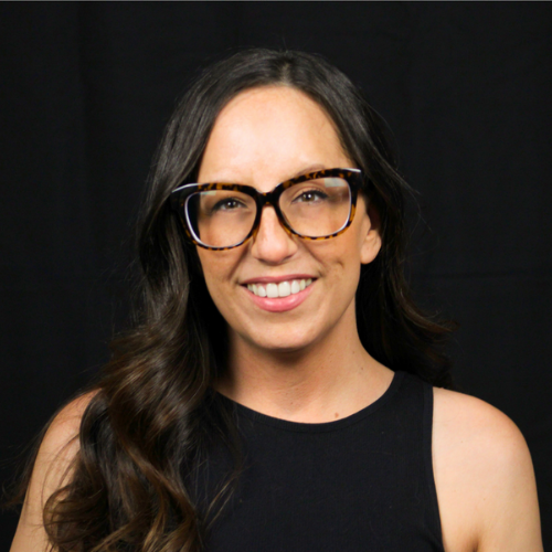 Woman with long dark hair, wearing glasses, smiling at the camera.