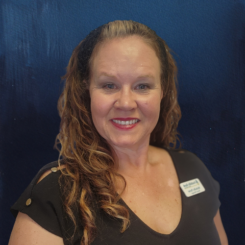 Woman with long wavy hair smiles, wearing a black top. Blue textured background.