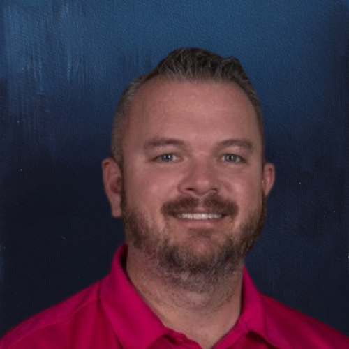 Man with beard smiles, wearing a pink shirt, set against a dark blue background.