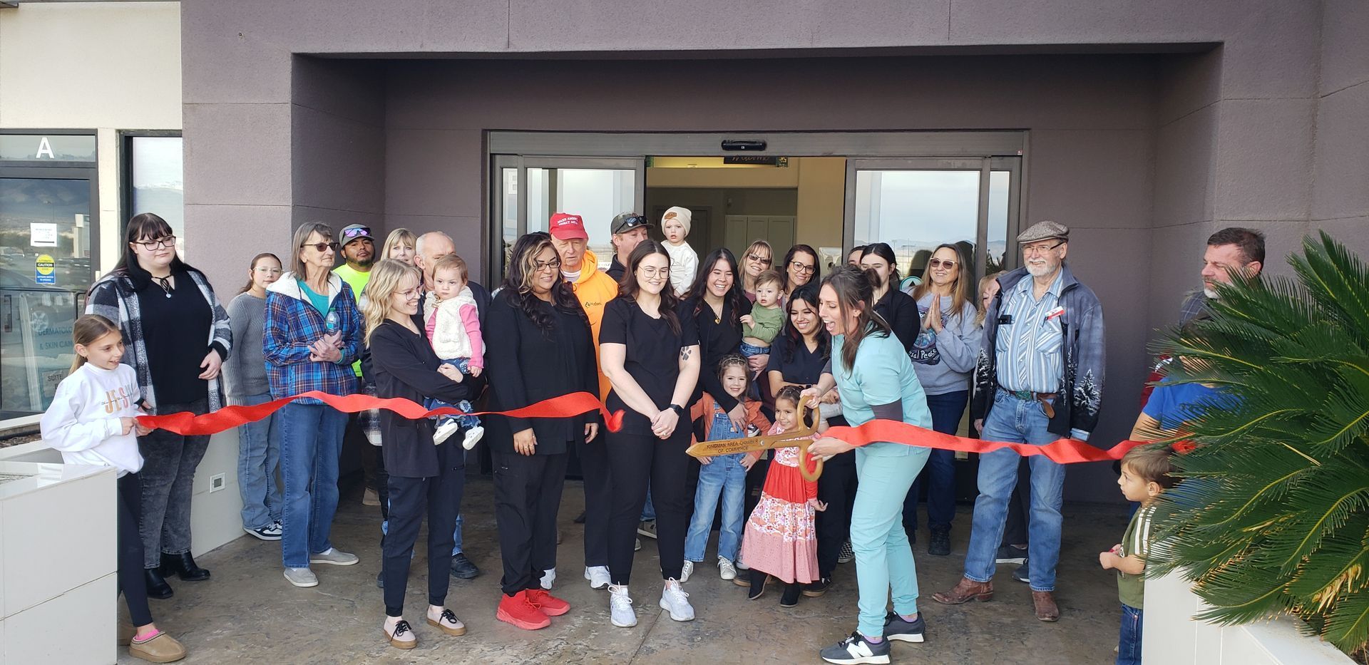 Group of people at a ribbon-cutting ceremony in front of a building with automatic doors.