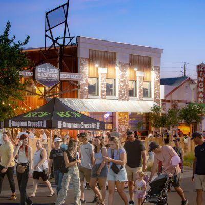 People walking and gathering outside businesses. Buildings in the background. Kingman CrossFit tent in the foreground.
