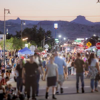 Crowd on a street lined with lights and tents, with mountain in background at dusk.