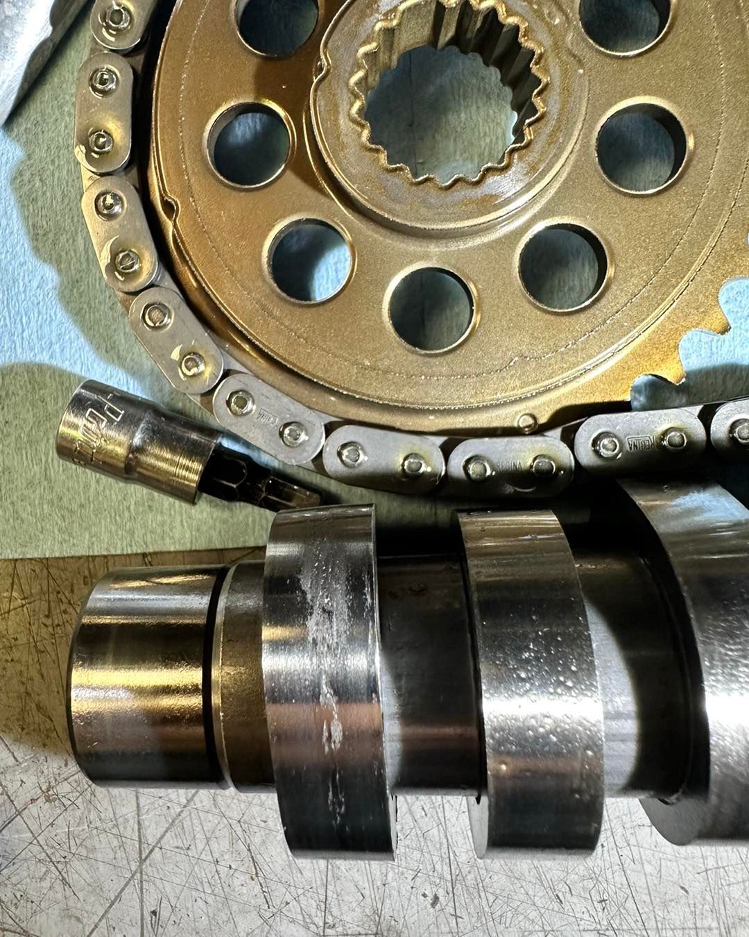 Engine parts: sprocket, timing chain, and camshaft with wear marks.