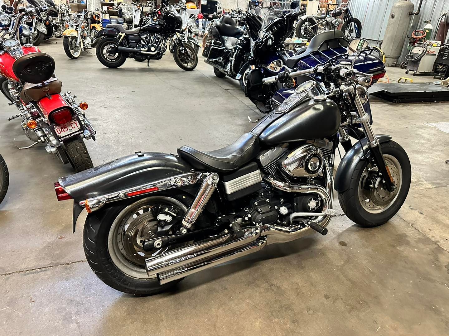 Black Harley-Davidson motorcycle parked in a showroom, chrome exhaust pipes, and black wheels.