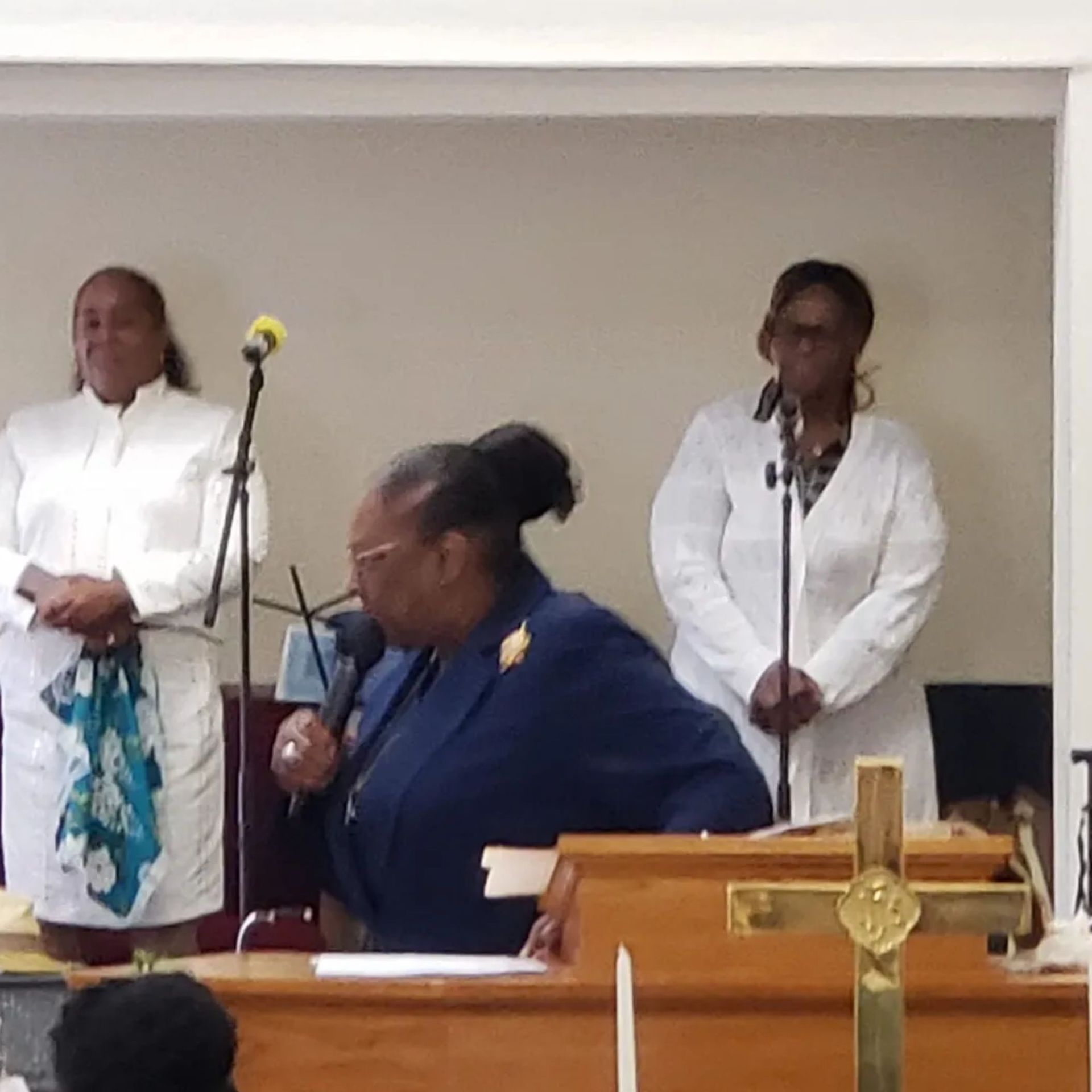 Three women are standing in front of microphones in a church