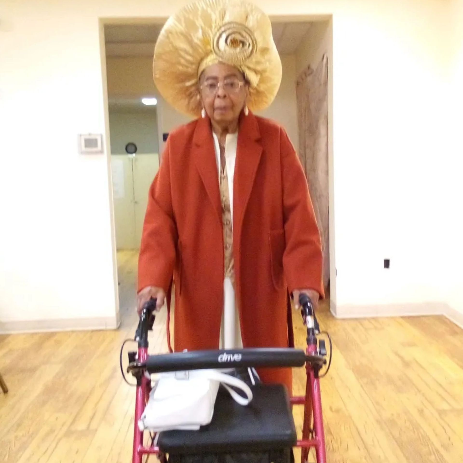 An elderly woman wearing a large hat is using a walker