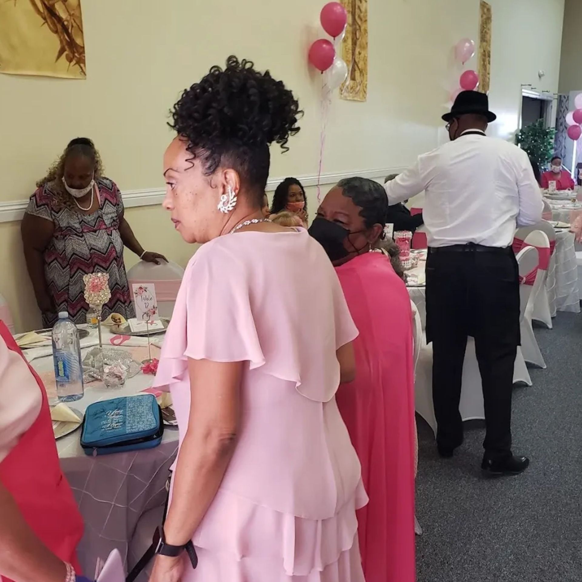 A woman in a pink dress is standing in a room with other people
