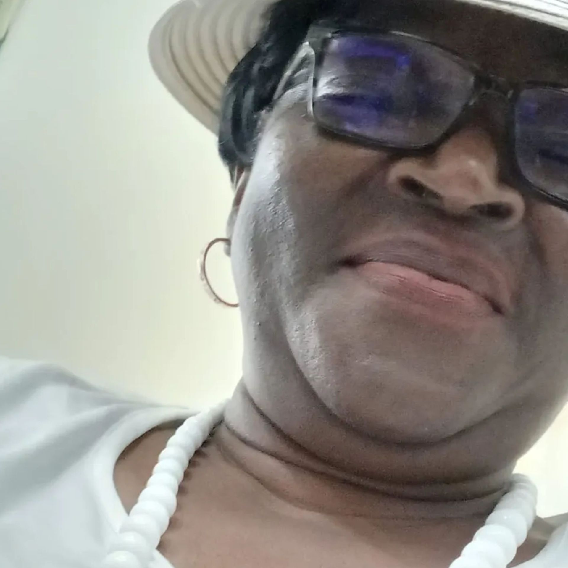 A woman wearing a hat and sunglasses is smiling for the camera