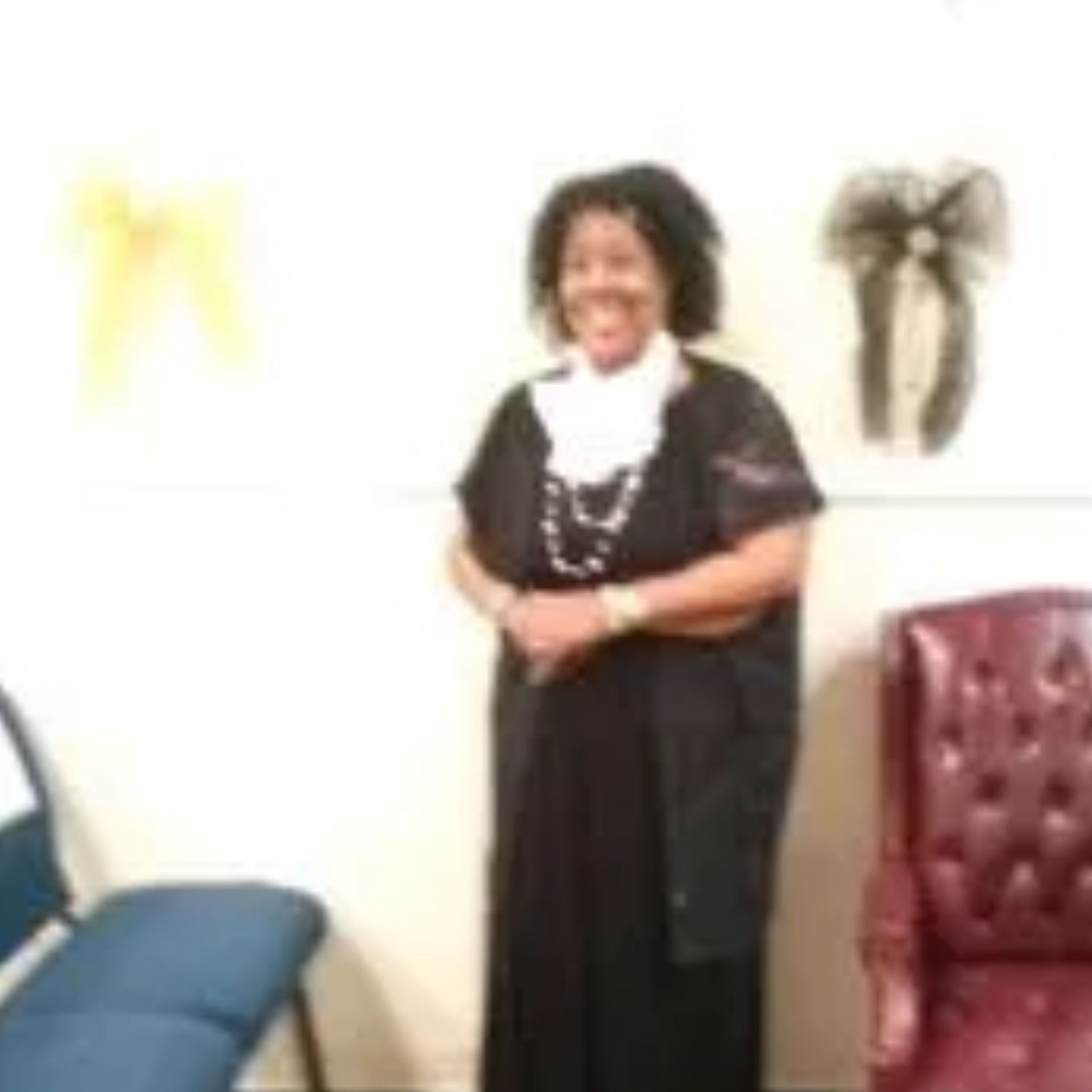 A woman in a black dress is standing in a room with chairs.