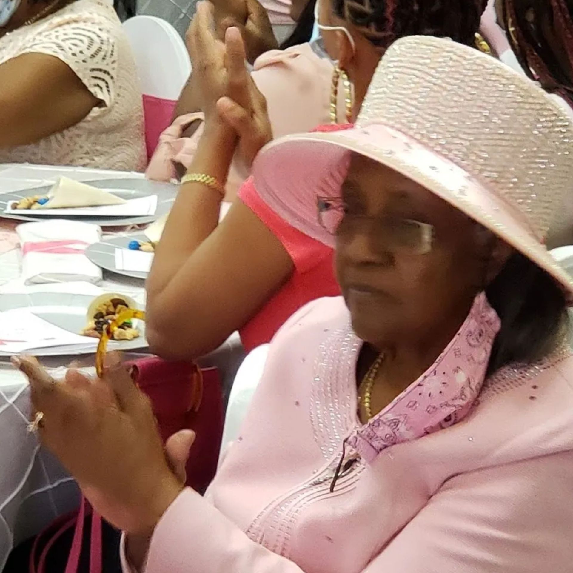 A woman wearing a pink hat and glasses sits at a table