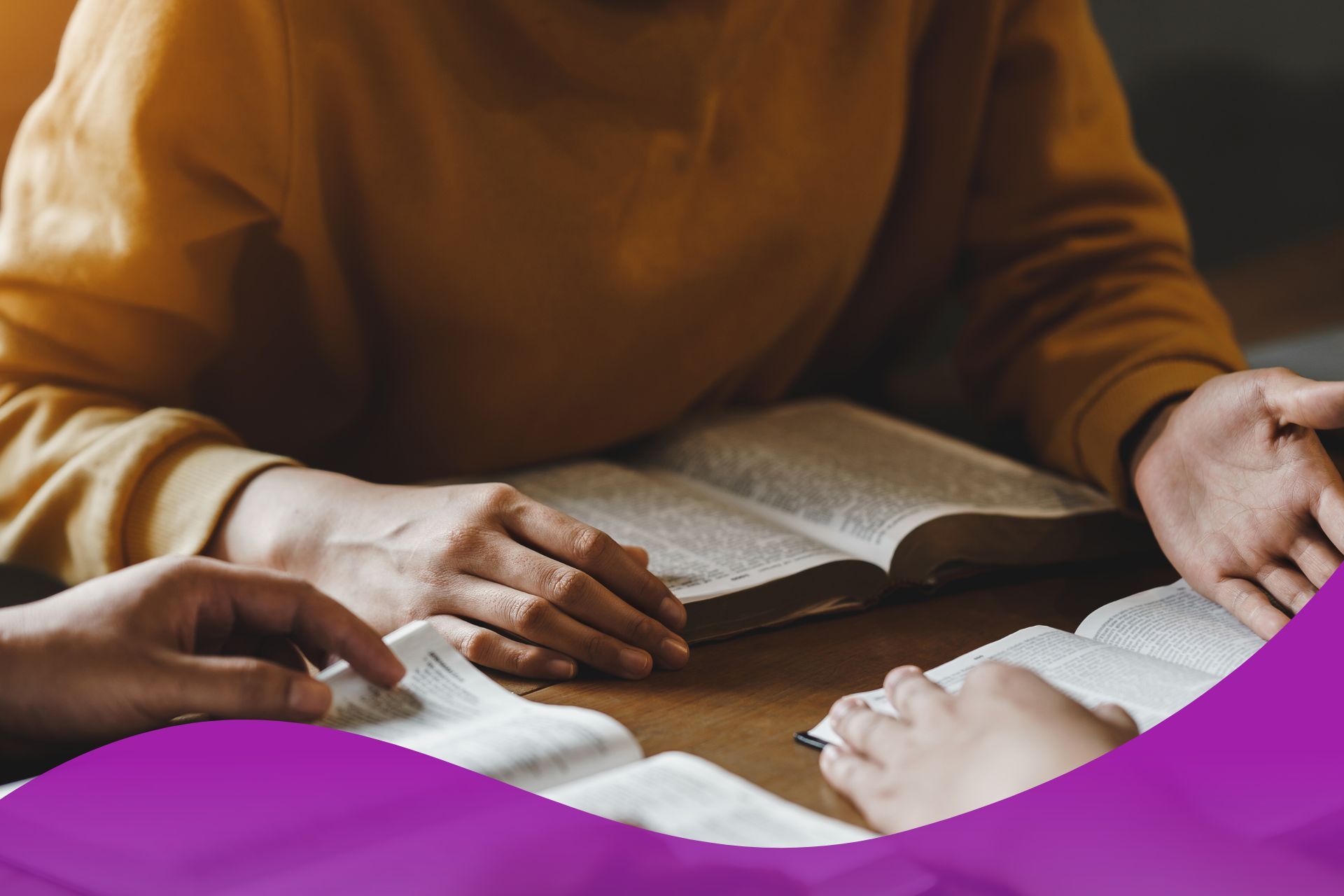 A group of people are sitting at a table reading a bible.