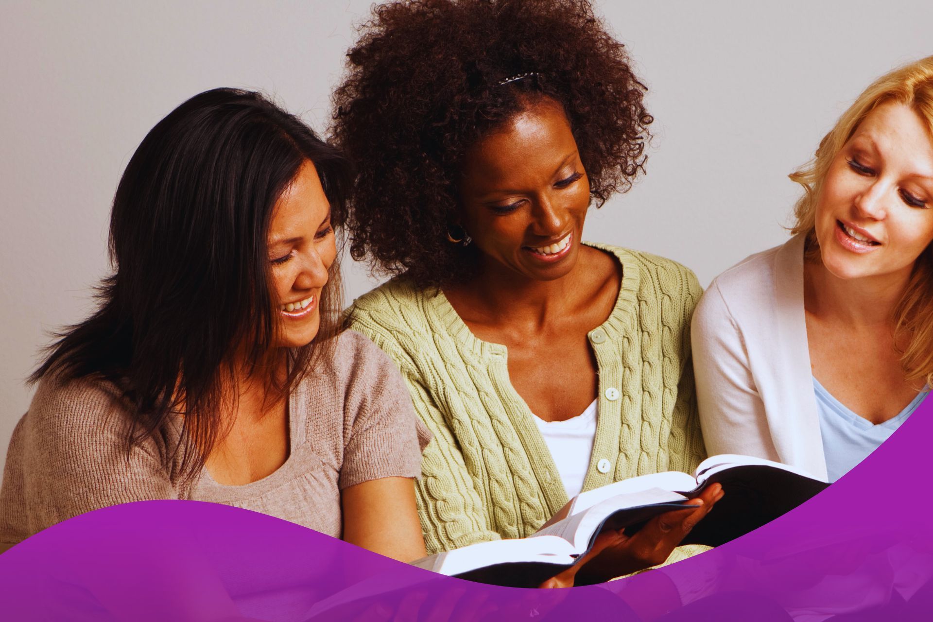 Three women are reading a bible together and smiling.